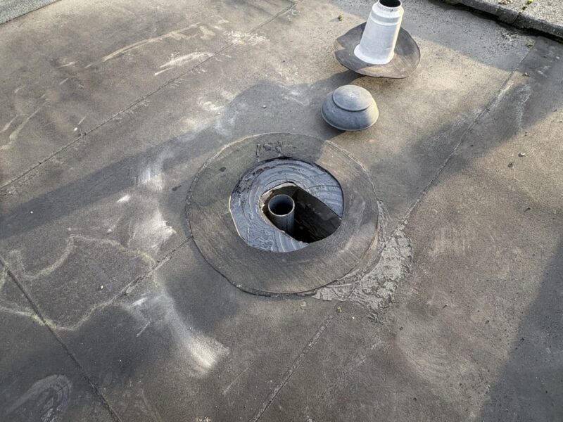 Uitgesneden dakdoorvoer op plat dak met zichtbare beluchtingsleiding en nieuwe ontspanningsdoorvoer naast de opening in Alphen aan den Rijn
