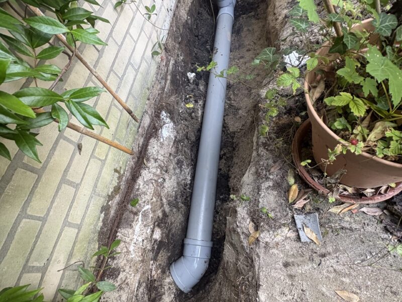 Nieuw aangelegde grijze PVC-rioolleiding met bochtstuk in opgegraven sleuf langs de gevel in Berkel en Rodenrijs
