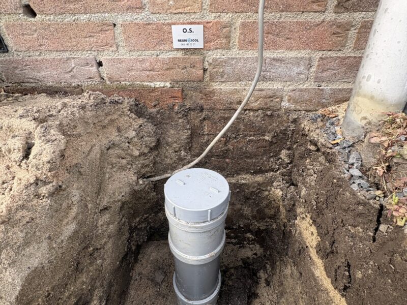 Opgegraven rioolleiding langs de gevel van een woning in Hendrik-Ido-Ambacht met nieuw PVC-buissegment en ontstoppingsstuk na reparatie door Regio Riool