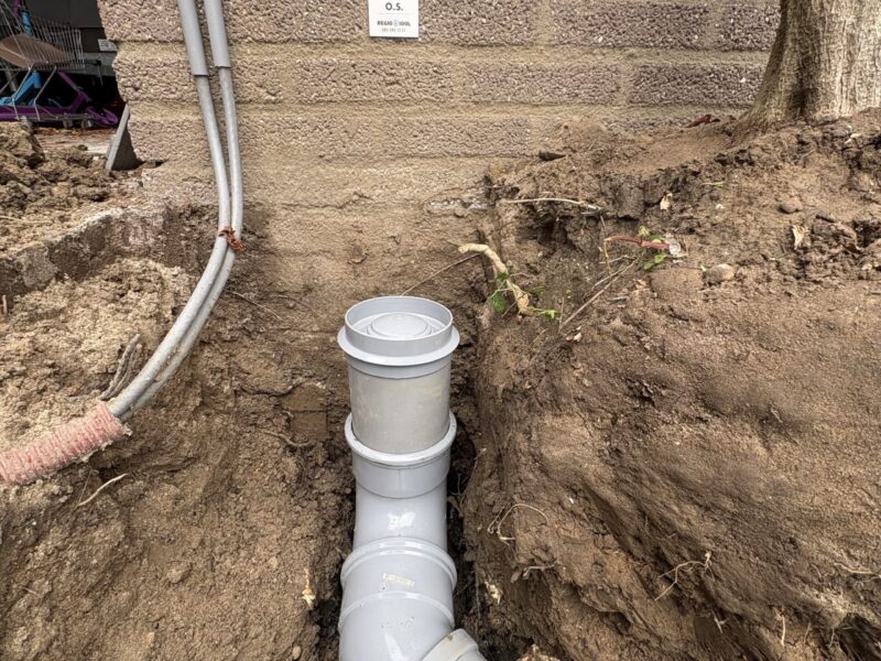 Detailopname van nieuw geplaatste PVC-riolering met ontstoppingsstuk naast gevel in Barendrecht, uitgevoerd door Regio Riool