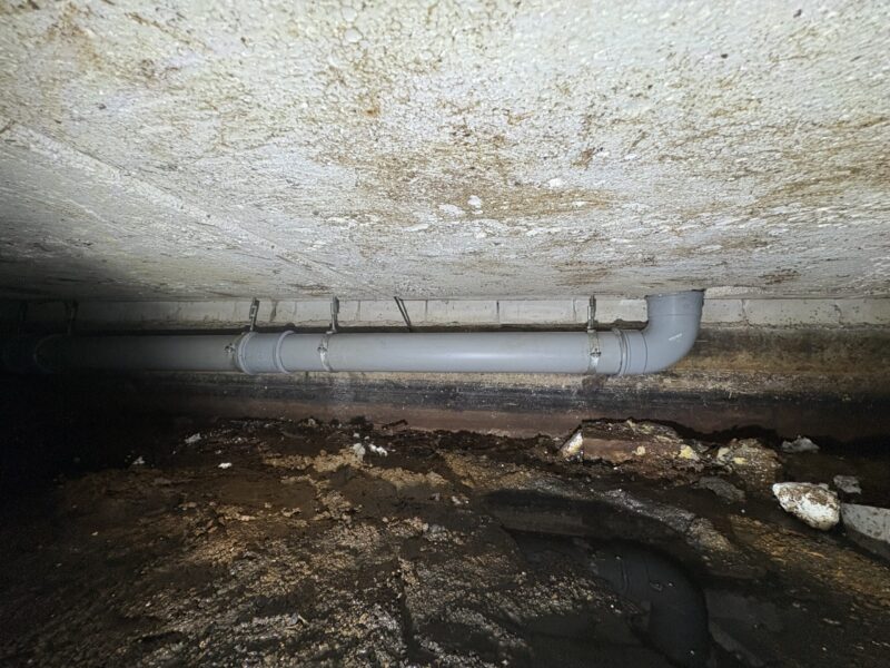 Vernieuwde grijze PVC-rioolleiding met beugels bevestigd aan de muur in de kruipruimte in Berkel en Rodenrijs